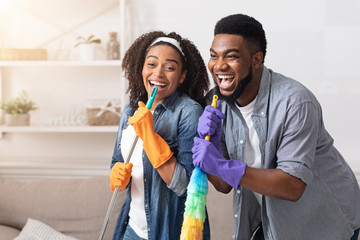 Housework with fun. African couple cleaning home together, singing and fooling