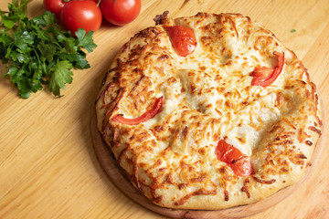 Georgian dish khachapuri with cheese and meat on a background of tomatoes and greens top view

