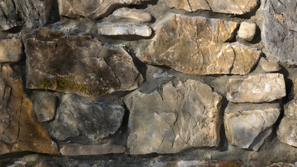 Fragment of a wall from a chipped stone at sunny day. The stones are arranged into layers of stone walls.
