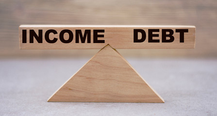 The concept of the balance of words between INCOME and DEBT on wooden scales on a light background