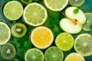 Large flat round slices of different fruits and citrus such as lime and lemon float together with kiwi, apple, orange and green leaves in water. The concept of juicy fresh fruits. Flat lay