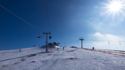 Top of mountain against blue sky at sunny day in the Carpathians. Ski lift is lifting people to top of mountain.