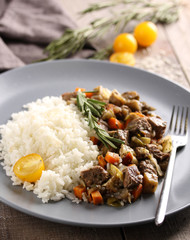 Healthy food. White rice with beef, vegetables and rosemary on a grey plate with a fork on a grey wooden background. Rustic. Yellow cherry tomatoes and herbs. Meat stew. Background image, copy space