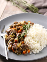 Healthy food. White rice with beef, vegetables and rosemary on a grey plate with a fork on a grey wooden background. Rustic. Meat stew. Background image, copy space