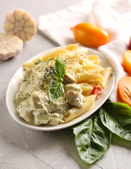 Italian cuisine. Penne pasta with chicken, cheese, basil and yellow tomatoes on a white plate on a light grey background. Healthy food. Garlic, spices and thyme. Background image, copy space