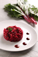 Healthy food. Beetroot rice with rosemary on a white plate on a light grey background. Beet tops. risotto. Red rice. Background image, copy space