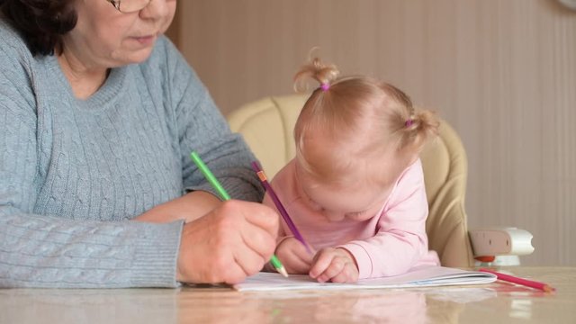 The child painstakingly draws with pencils in the album, bending over the paper, sitting next to her grandmother. Nanny and baby. Selective focus