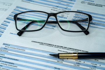 Fountain pen and eyeglasses on a quarterly corporate financial report waiting for the financial and investment analyst to analyse before public disclosure. Financial investment analysis concept.