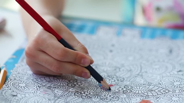 Antistress coloring page. Child  hand paints a coloring book for adults with crayons.