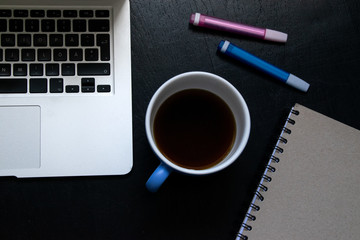 View from above of modern workplace with cup of tea, laptop, pens and notebook on black wooden table