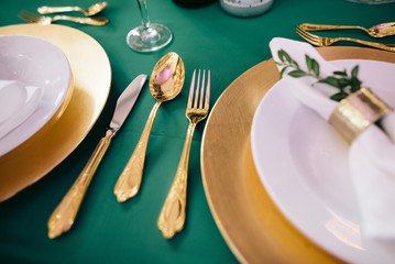 Tables for wedding party serving with plates and napkins, and decorated with greenery and gold and green cutlery