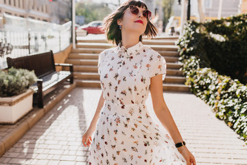 Attractive stylish woman in elegant dress enjoying summer in weekend. Outdoor photo of relaxed brunette girl in sunglasses walking around city in spring day.