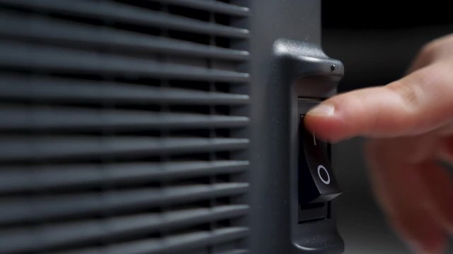 finger of a person presses turns on and off on a black plastic button a swing printer device with a radiator