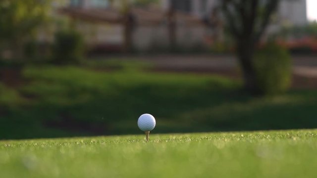 Golf club hits a golf ball in a super slow motion. Drops of morning dew and grass particles rise into the air after the impact