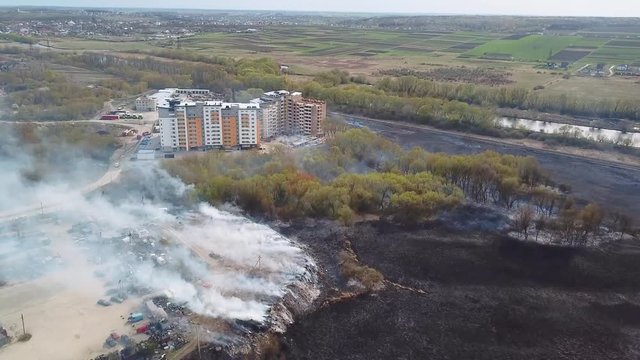 Aerial view of big smoke clouds and fire on the field. Aerial drone flight over burning hill side with thick white smoke blown off frame