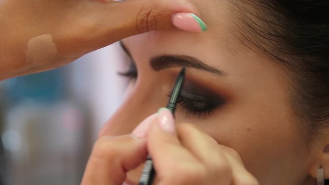 Draw the brow line with a makeup pencil. Make-up artist doing makeup for the young girl, close-up.