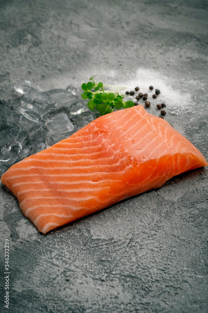 Wall mural fresh natural raw salmon fillet on ice cut into steak on a stone background with seasonings and herb