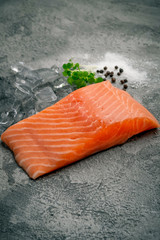 Fresh natural raw salmon fillet on ice cut into steak on a stone background with seasonings and herbs