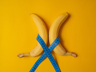 Two bananas in the form of a waist with a measuring tape on an orange background. The concept of...
