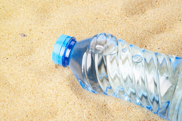 Fototapeta na wymiar Blue plastic bottle with drinking water on a yellow sea sand. Concept of thirst, hot summer weather, sea holiday and vacation on a beach.