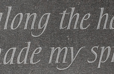 Close up of ornate chiselled letters carved from dark grey grainy slate shot straight on.