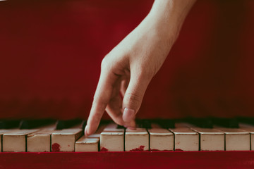 a close-up of a side view with female hand with pink manicure playing the piano. An old red piano with black and white keys. A palm above the keyboard. Graceful fingers of composer or musician