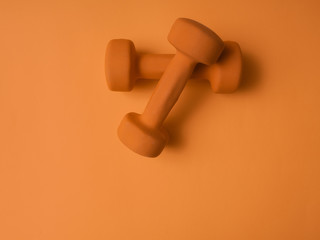 Orange dumbbells for fitness on an orange background. Minimalism. Place for text. Sport concept. Flat lay.