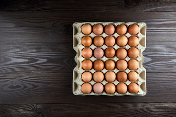 Chicken eggs in recycled cardboard tray on brown wooden table, top view