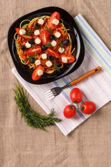 A black plate with spaghetti in a sauce decorated with cherry tomatoes olives and mozzarella on a linen napkin. Save a place.