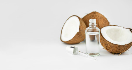 Coconut oil in a bottle with coconuts on a white background. Skin care concept. Face cosmetics. Banner. Copy space.
