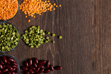 three types of legumes, beautifully laid out in cups and on a wooden background - red beans, green peas and orange lentils. Top view. copy space.