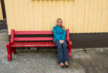 Young woman sitting alone on a red bench yawning.