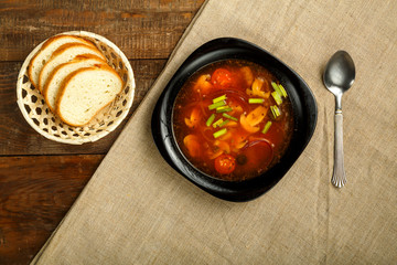 black dish of italian tomato soup with potatoes and mushrooms on a wooden table on a napkin and a spoon and bread.
