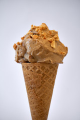 Peanut butter banana ice cream cone with sprinkles of peanuts on top on a white background - gluten-free waffle cone 