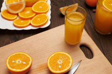 Fresh orange fruit whole and sliced on a wooden table, cutting board and kitchen knife. A plate full of citrus slices - natural and healthy food. Glass of fruit cocktail.