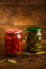 Jars of pickled homemade pickled cherry tomatoes gherkins on a wooden table. Vertical