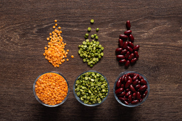 three types of legumes, beautifully laid out in cups and on a wooden background - red beans, green peas and orange lentils. Top view. copy space.