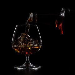 Pouring whiskey drink into glass with ice cubes