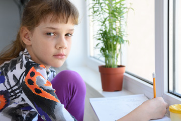 Girl spending time at home in quarantine, girl draws while sitting by the window