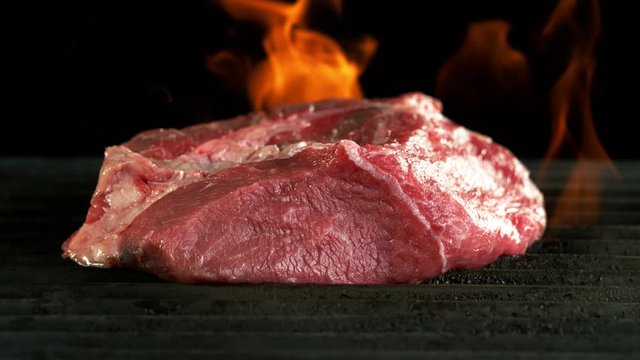 Super slow motion of raw beef steak on grill with fire, isolated on black background. Filmed on high speed cinema camera, 1000 fps