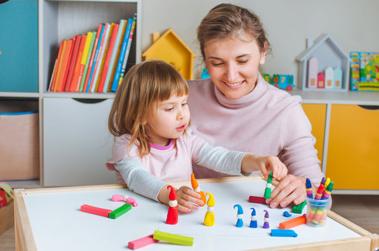 Happy mother and little four years old girl molding colorful gnomes in the room