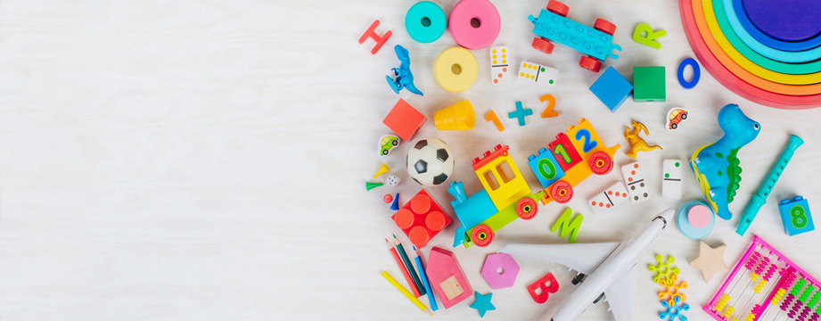 Variety of plastic and wooden kids toys on light wooden background with copy space