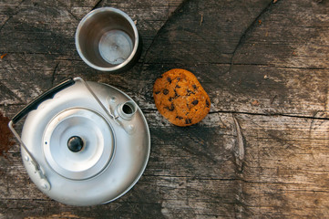 Aluminum teapot , cup and oatmeal cookies with chocolate on dry wooden table. Flat lay food. Picnic. Outdoor cooking. Kettle 