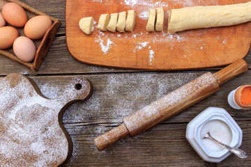 Making homemade pasta pici. Sliced rolled dough for pasta and prepared long pasta on black slate board with flour and egg shell over old wooden table. Dark rustic style.