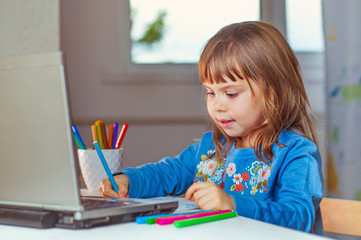 Happy little four years old girl doing homework using the notebook for distance learning