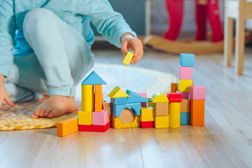 Close up of little girl playing with colorful wooden brickes on the floor