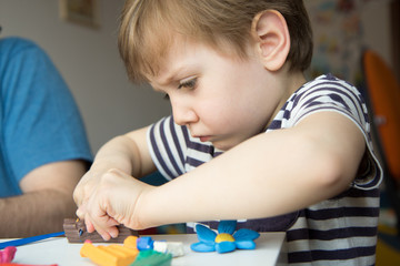 Reportage portrait of a child who cuts plasticine for modeling. Development of fine motor skills with the whole family.