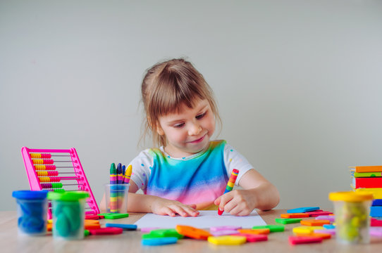 Happy little four years old girl drawing with wax crayon sitting at the table