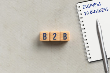 cubes with acronym B2B and notepad with explanation BUSINESS TO BUSINESS on paper background