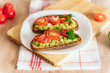 toasted bread with avocado paste and fresh tomato. Avocado mixed with lemon juice is spread on bread.  health food concept, vegan, vegetarian